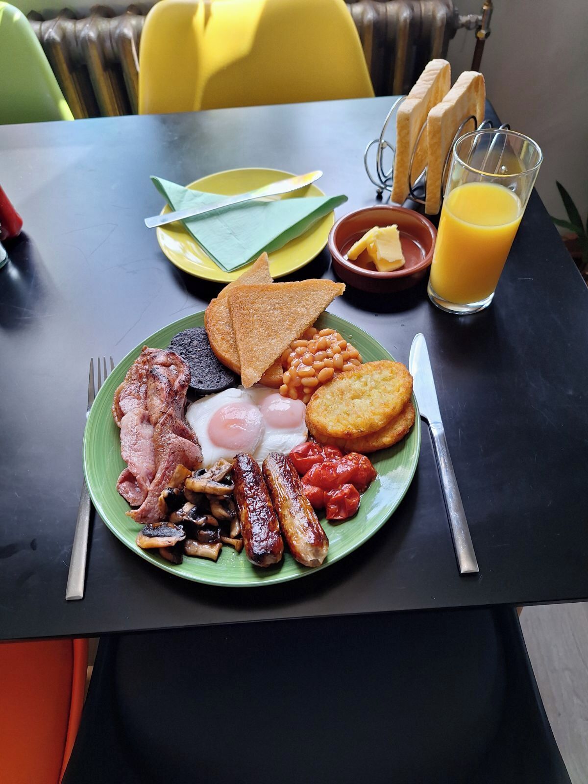 A breakfast plate with bacon, eggs, sausages, beans, toast, and tomatoes.