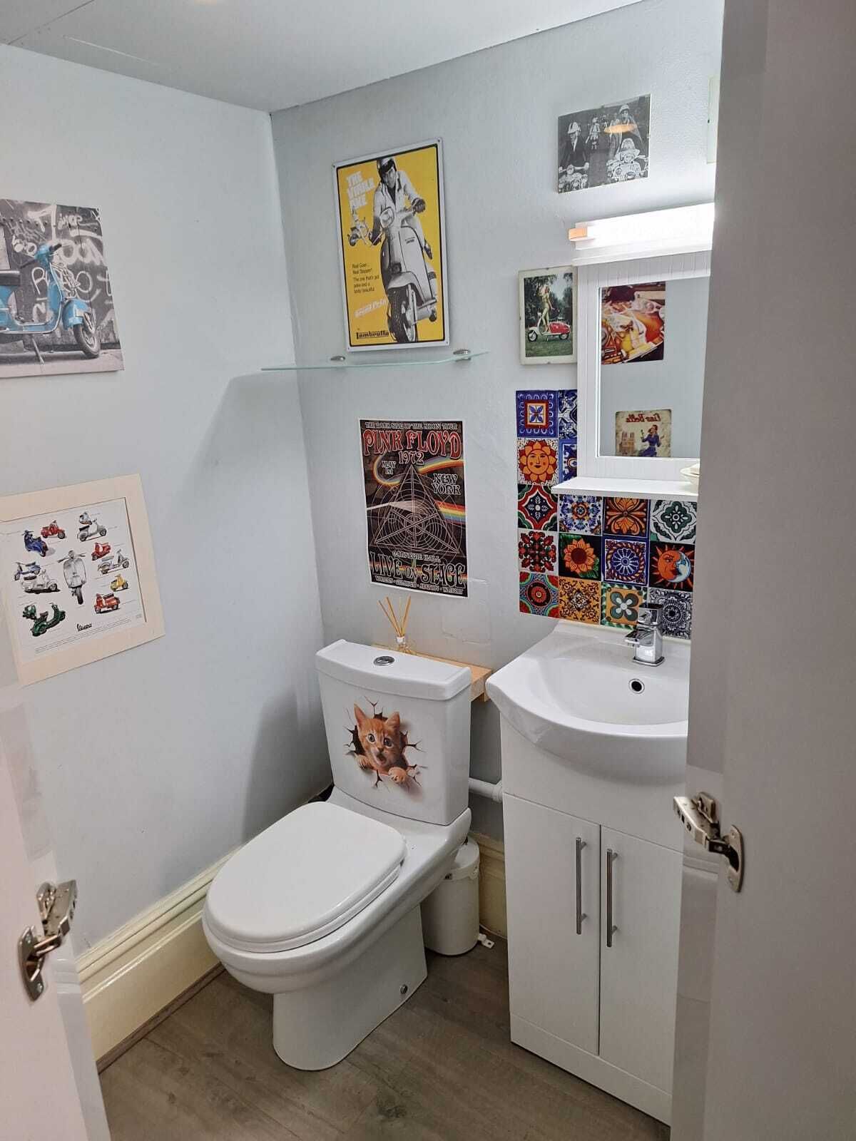 A bathroom with a toilet, sink, and cabinet. There are posters and tiles on the walls.