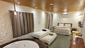 Une chambre dotée d’une grande baignoire, de deux lits, d’une coiffeuse en bois et de murs à l’aspect pierre.