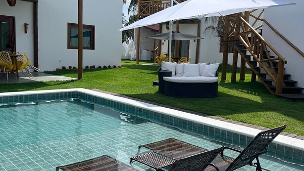 Un espace piscine comprenant des chaises longues, un coin salon couvert et un escalier menant à un niveau supérieur.