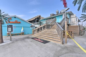 A blue building with a sign reading "Sandbar" and a wooden staircase leading to a deck.