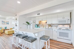 A modern kitchen with white cabinetry, a central island with stools, and a built-in oven and microwave.