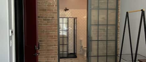A bedroom with a brick wall, a sliding door, a bed, and a metal shelf.