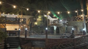 An outdoor area with a stone wall, palm trees, and string lights. - Coastal Haven Resort (San Juan)