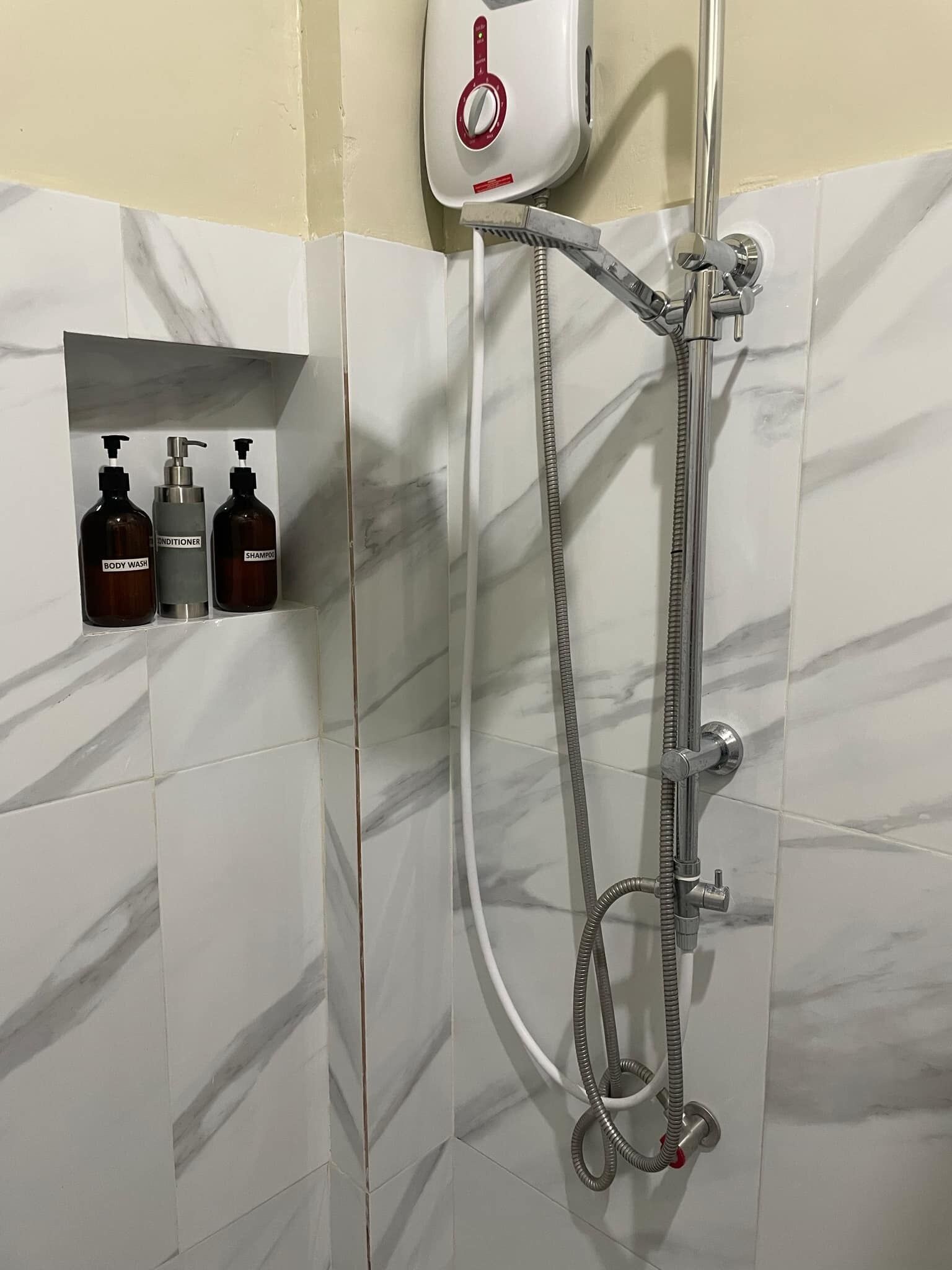 A shower with a handheld showerhead and a handheld hose. There is a control panel above the shower.