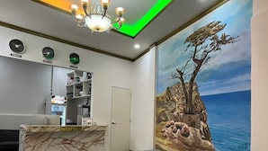 A reception area with a marble counter, a clock, a chandelier, and a mural of a tree by the sea. - Coastal Haven Resort (San Juan)