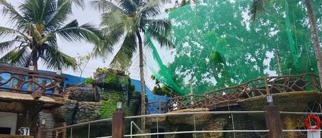 A tropical resort with a stone bridge, palm trees, and a large green net structure.