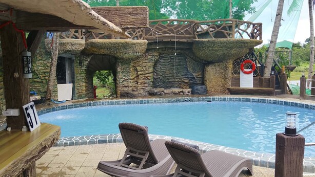 A pool area with lounge chairs, a wooden deck, and a stone wall with a cave-like structure. - Coastal Haven Resort (San Juan)