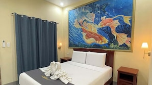 A hotel room with a bed, a painting of fish on the wall, a curtain, a nightstand, and a lamp. - Coastal Haven Resort (San Juan)