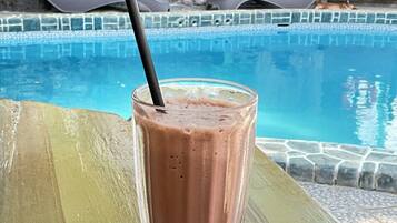 A glass of chocolate milkshake with a straw on a white plate by a poolside.