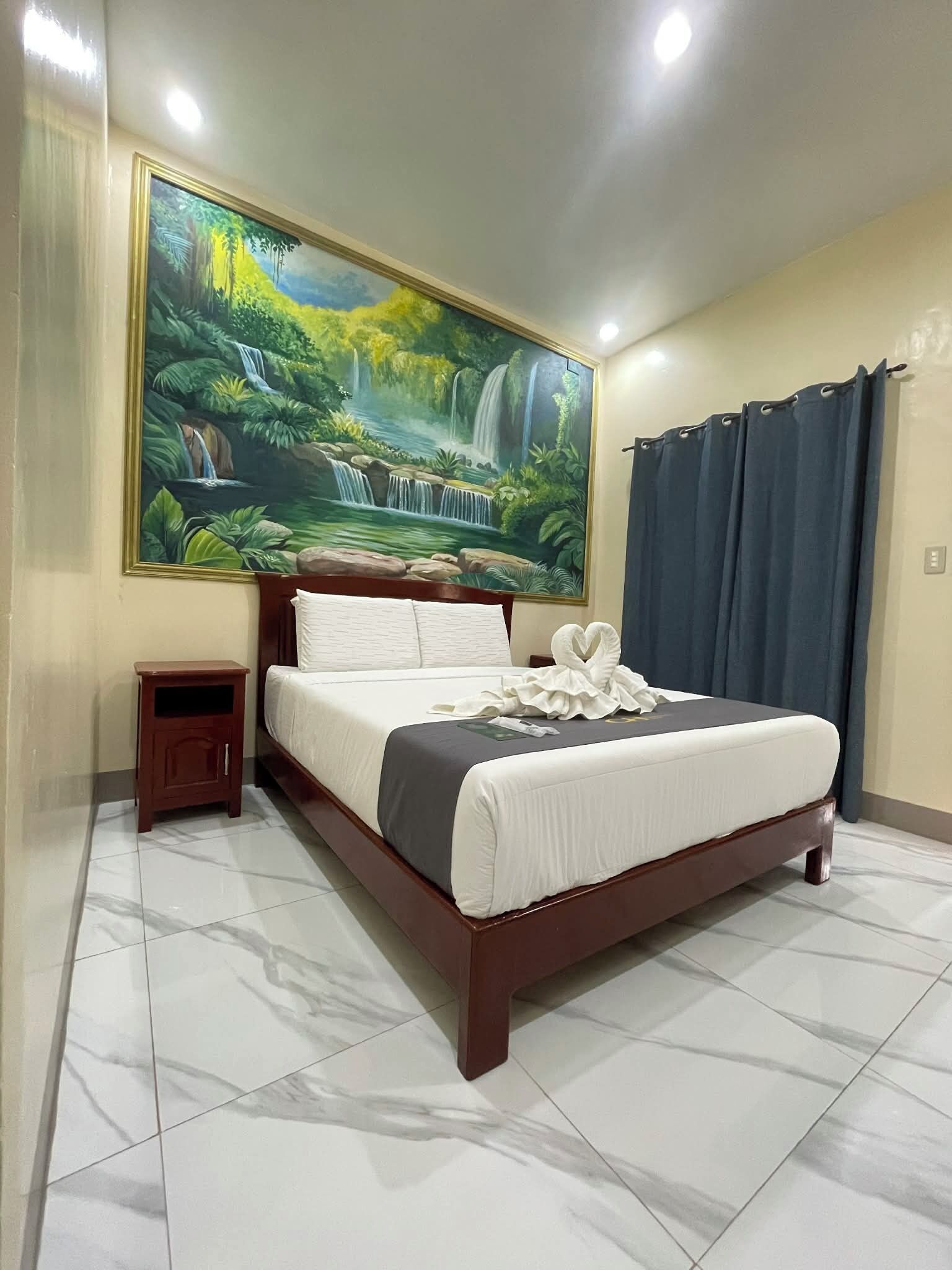 Quarto de hotel com uma cama grande, uma mesa de cabeceira, um quadro de uma cachoeira e uma cortina.