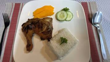 A plate with grilled meat, white rice, mango slices, and cucumber slices.