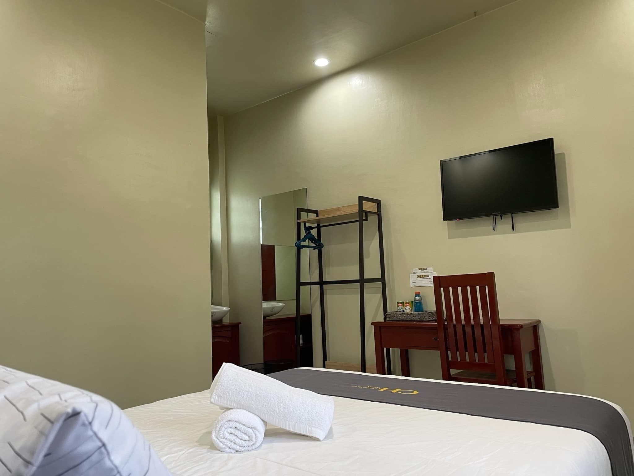 A hotel room with a bed, a desk, a chair, a TV, and a mirror.