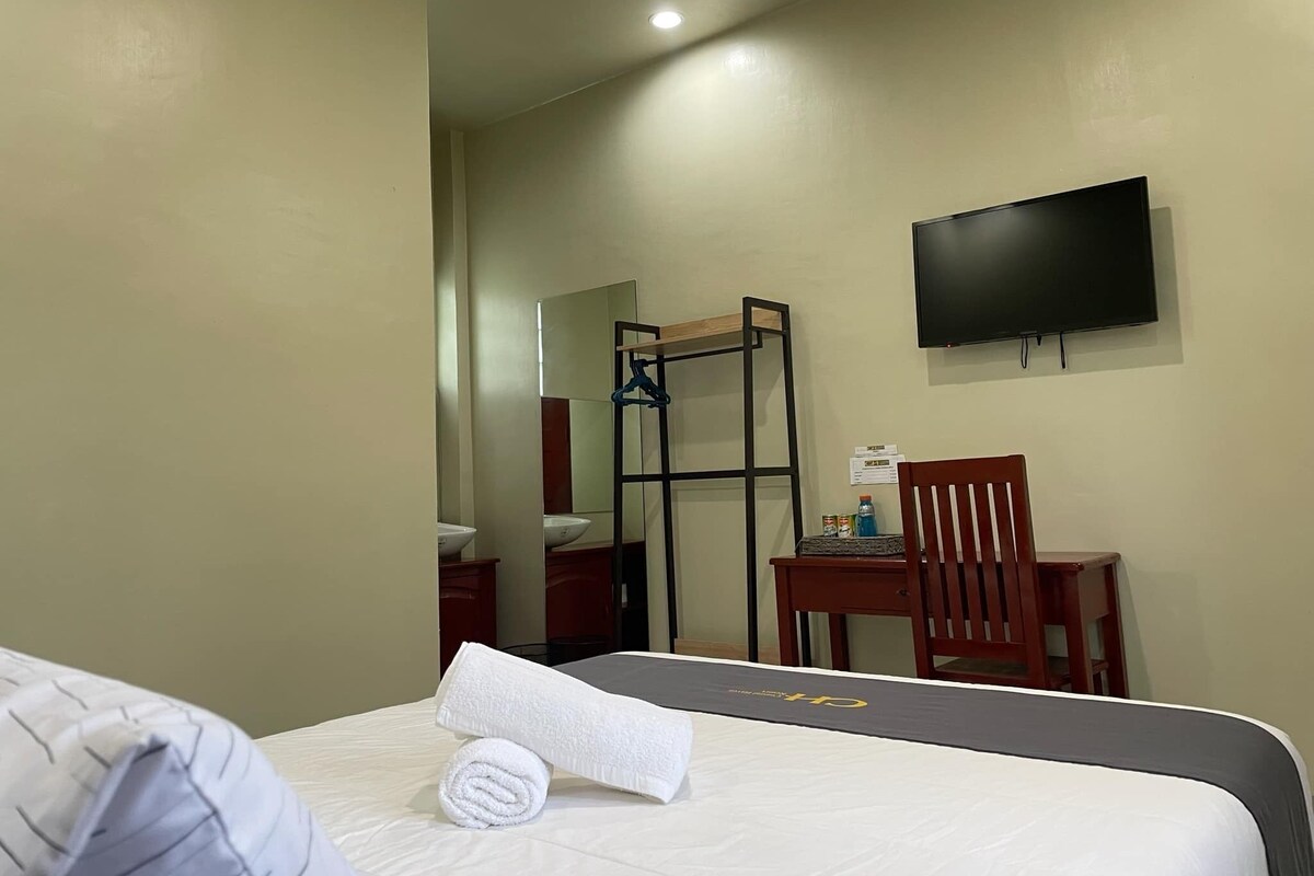 Ein Hotelzimmer mit Bett, Schreibtisch, Stuhl, Fernseher und Spiegel.