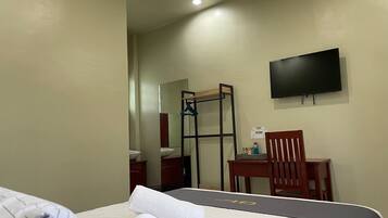 A hotel room with a bed, a desk, a chair, a TV, and a mirror.