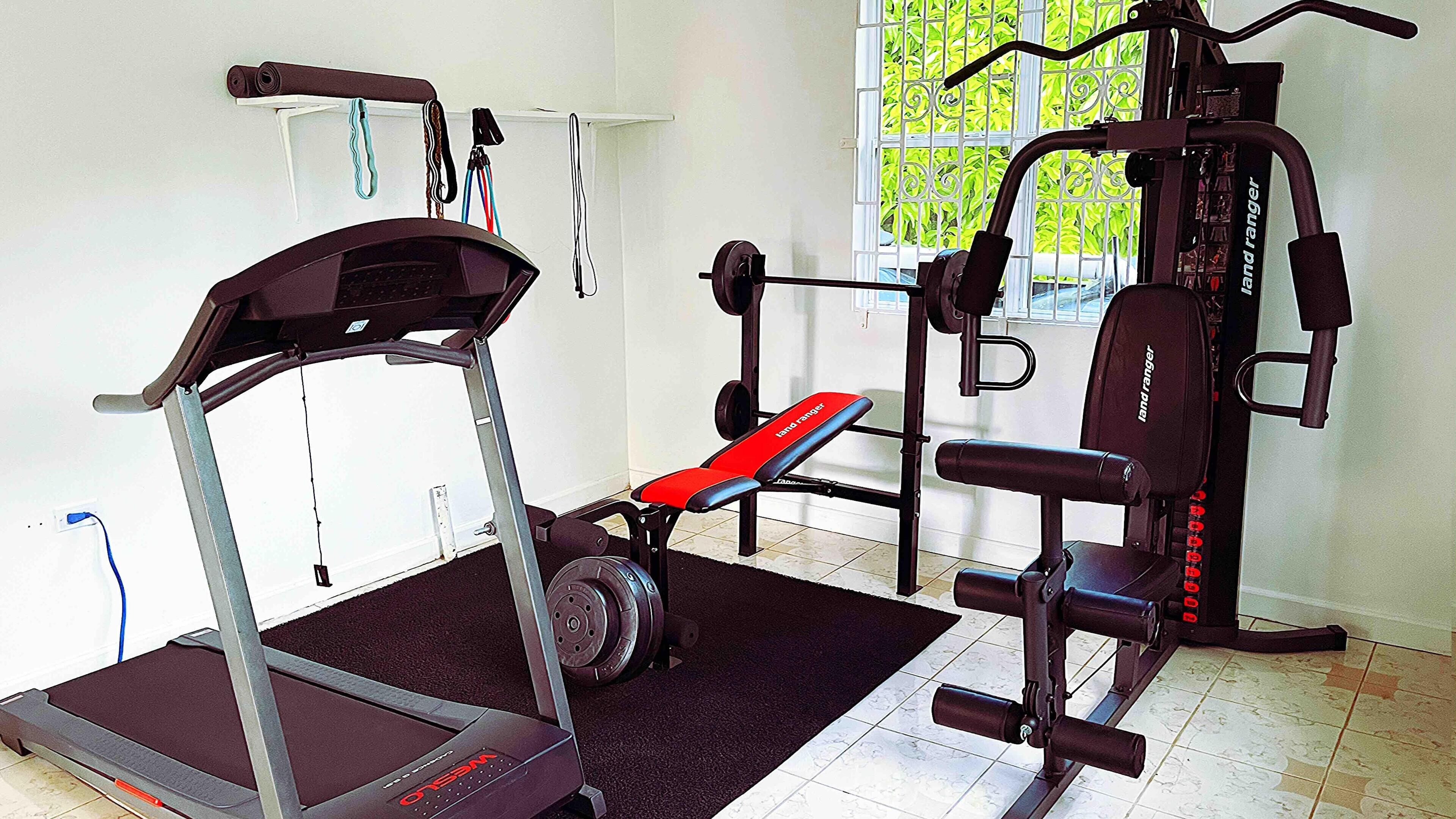 A home gym with a treadmill, bench press, and weight bench.