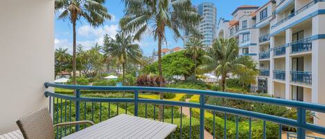 A balcony with a view of a landscaped garden, palm trees, and hotel buildings.