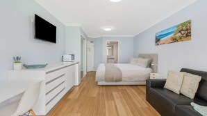 Une chambre moderne avec un lit, une télévision, un bureau doté d’un micro-ondes, un canapé en cuir noir et un tableau accroché au mur.