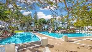 Un espace piscine comprenant plusieurs piscines, des chaises longues et un jardin aux allures tropicales.
