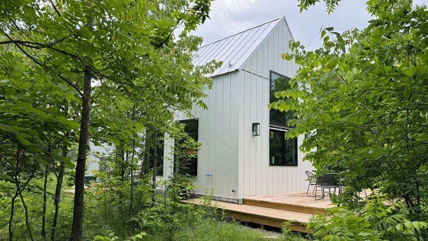 Un edificio moderno blanco con techo inclinado, rodeado de abundante vegetación y árboles.