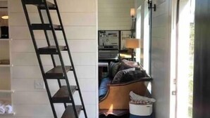 Un pasillo estrecho con una escalera de madera, un sofá y un cubo de basura.