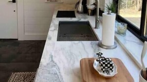 Una cocina moderna con encimera de mármol, un lavamanos, un ventanal con vistas y una tabla de cortar de madera decorativa.