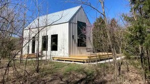 Un pequeño edificio de una sola planta con techo de metal y terraza de madera, rodeado de árboles.