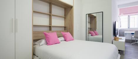 A bedroom with a bed, a wardrobe, a desk, and a mirror.