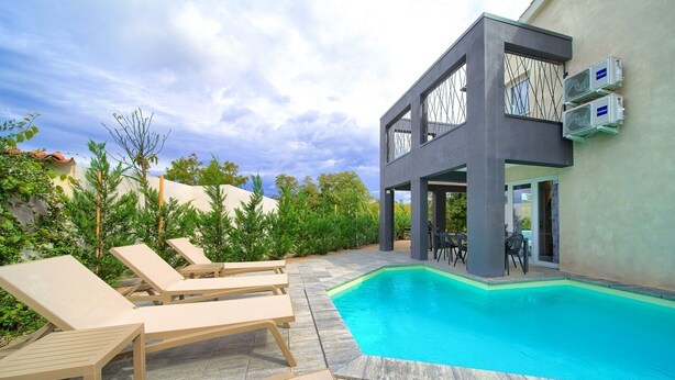 A modern poolside area with lounge chairs, a swimming pool, and a building with large windows and air conditioning units. - Villa Melody with heated pool and sauna (Kvarner - Sveti Ivan Dobrinjski) (Sveti Ivan Dobrinjski)