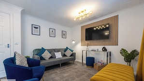 A modern living room with a grey sofa, blue armchairs, and a yellow ottoman. - Comfy House - Sleeps 14 - 14 min to City Centre (Manchester)