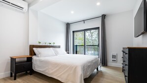 A modern bedroom with a bed, a nightstand, a dresser, and a TV. - Cozy Modern Cottage - Walking distance to 5 beach access points (Tiny)