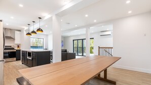 A spacious kitchen with modern appliances, a dining area with a long table, and a view of the outdoors. - Cozy Modern Cottage - Walking distance to 5 beach access points (Tiny)