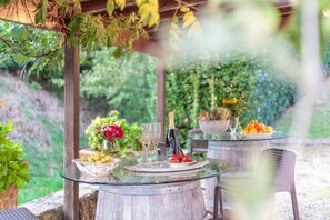 Un tavolo in vetro con una bottiglia di champagne, bicchieri, una ciotola di frutta e un vaso di fiori.