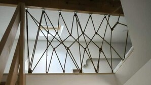 Un escalier doté d’une rampe métallique aux motifs géométriques mène à une mezzanine. Trois œuvres d’art encadrées sont accrochées au mur en contrebas.