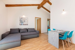 Una sala moderna con un sofá seccional gris, un comedor con sillas azules y piso de madera.