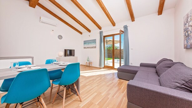 Ein modernes Wohnzimmer mit Holzbalkendecke, einem grauen Sofa und einem Essbereich mit blauen Stühlen und einem Holztisch.