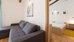 Ein modernes Wohnzimmer mit einem Ecksofa, einem Bett mit Holz-Kopfteil und einem kleinen Tisch.