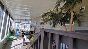 A covered outdoor area with a wooden railing, a palm tree, and a table with chairs. - The Red Sisters Retreat.  (Edgewater)