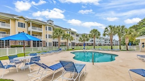 A pool area with lounge chairs and umbrellas, surrounded by a white fence and palm trees. - Myrtlewood Top floor Condo 2BR • 4 Beds • 2 full Baths • with Elevator (Myrtle Beach)