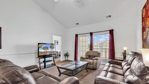 A living room with leather sofas, a glass coffee table, a flat-screen TV, and a large window with red curtains. - Myrtlewood Top floor Condo 2BR • 4 Beds • 2 full Baths • with Elevator (Myrtle Beach)