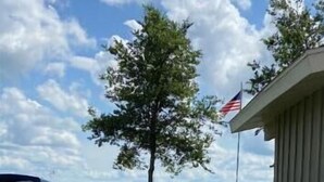 A house with a flag, a lawn, and a body of water in the background. - Escape to this peaceful lakefront getaway on Lake Hendricks (White)