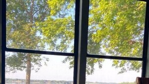 A room with a large window overlooking a lake, a wicker table with a blue mug, and a wicker chair. - Escape to this peaceful lakefront getaway on Lake Hendricks (White)