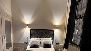 Une chambre à coucher avec un grand lit, deux tables de chevet, une petite table ronde et deux fauteuils.