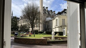Une cour avec une statue, un grand arbre et un bâtiment à l’architecture classique.