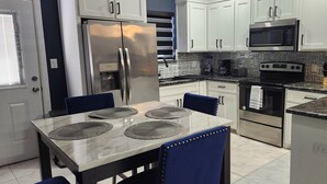 Una cocina moderna con armarios blancos, electrodomésticos de acero inoxidable, encimera de granito y una zona de comedor con sillas y manteles individuales azules.