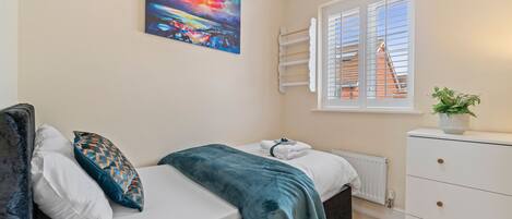 A bedroom with a bed, a window with blinds, a radiator, a dresser, and a painting on the wall.