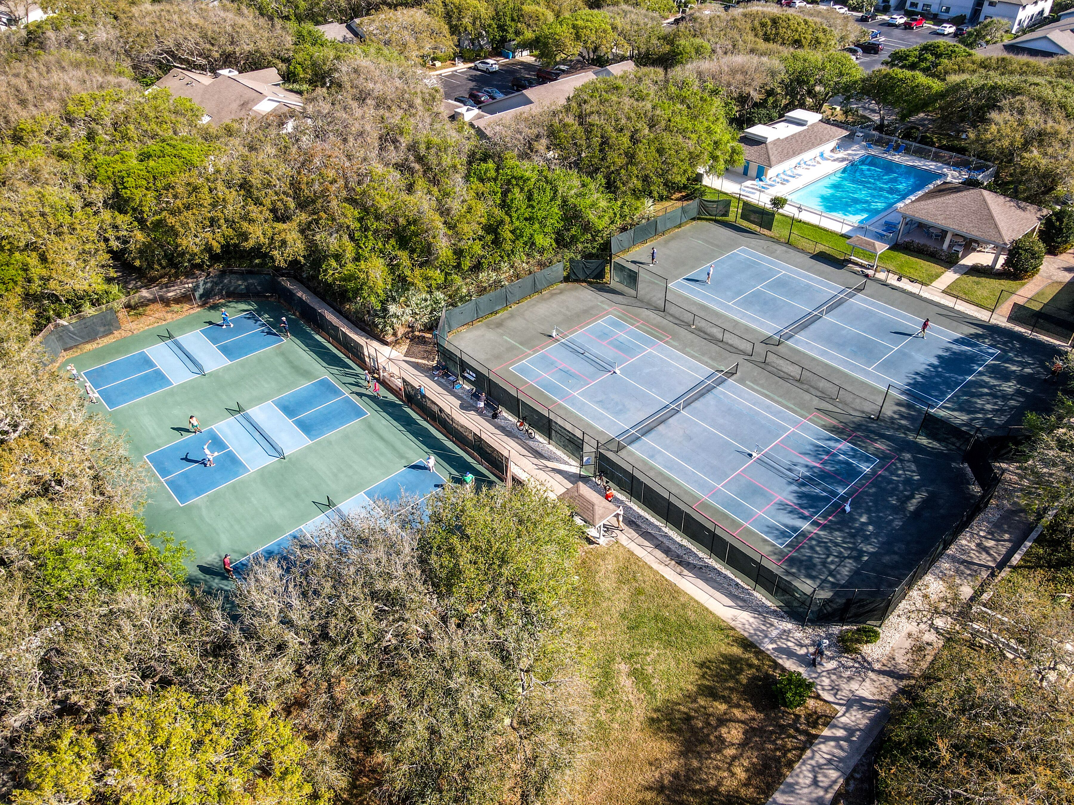 Eine Luftaufnahme eines Wohngebiets mit mehreren Tennisplätzen, einem Schwimmbad und umliegender Bepflanzung.