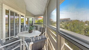 Un espacio de estar al aire libre cubierto con mesa y sillas, ventanas amplias y vistas a zonas verdes y edificios.