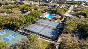 Vista aérea de una zona residencial con una piscina grande, canchas de tenis y acceso a la playa.