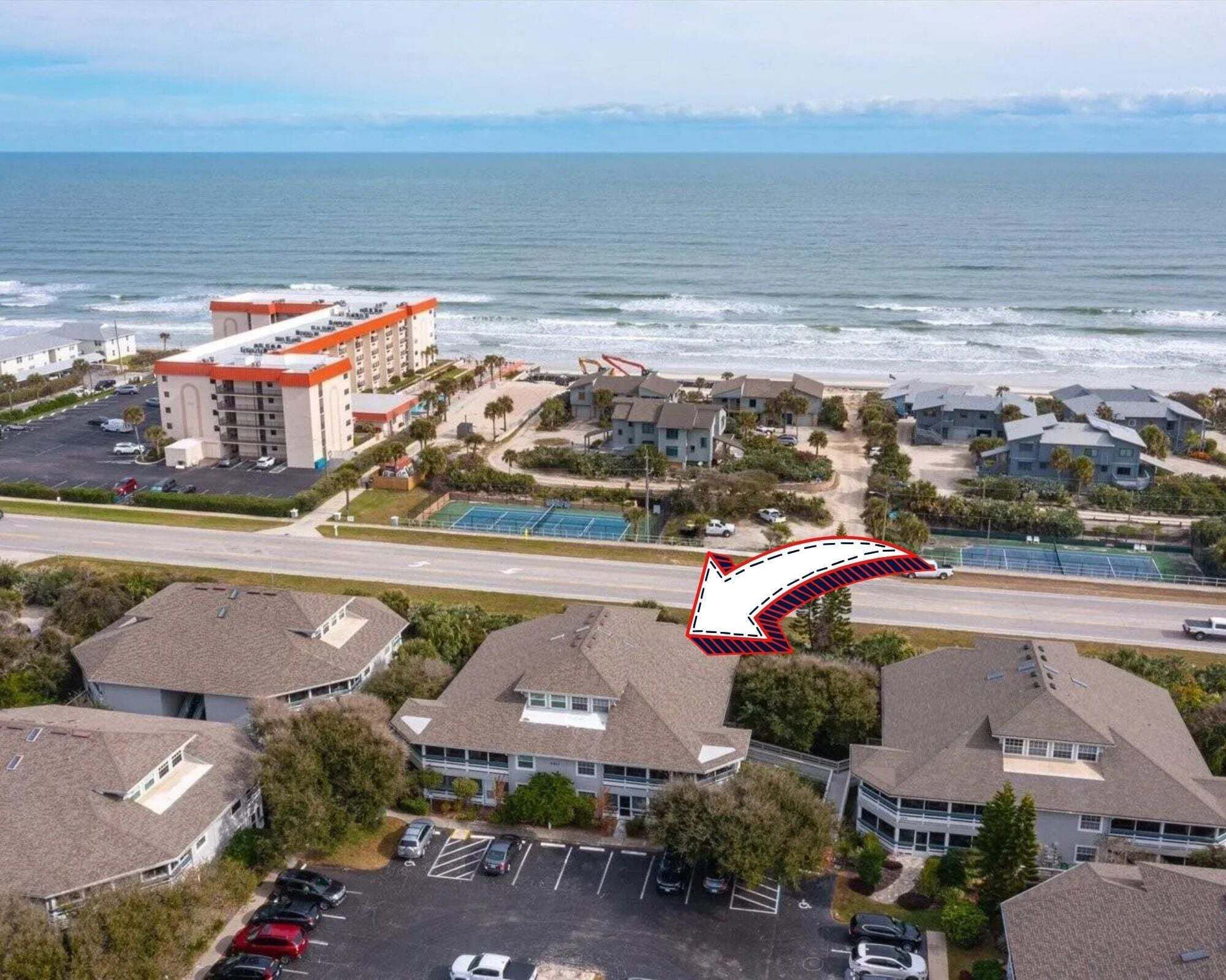 An aerial view of a coastal residential area with a hotel, parking lots, and a beach.